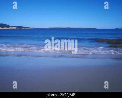 Un'esposizione panoramica di calme onde del mare che colpiscono la costa con sabbia liscia Foto Stock