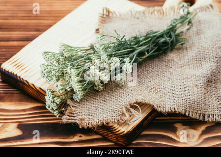 Achillea millefolium, yarrow o yarrow comune fiori freschi bianchi su un tagliere di legno pronto per la cottura di medicinali, farmaci o essiccazione Foto Stock