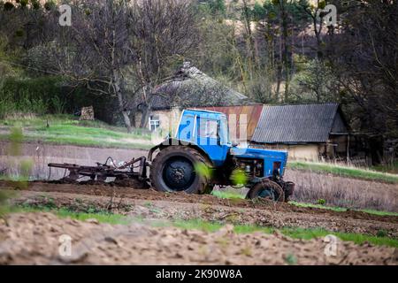 vecchio trattore blu con aratro sul campo e coltiva il terreno. Preparando il suolo per piantare vegetali in primavera. Macchine agricole, lavoro sul campo. Foto Stock