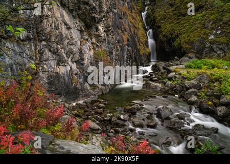 Un lungo scatto di esposizione di una piccola cascata nel bosco circondato da rocce ricoperte di muschio, Norvegia Foto Stock