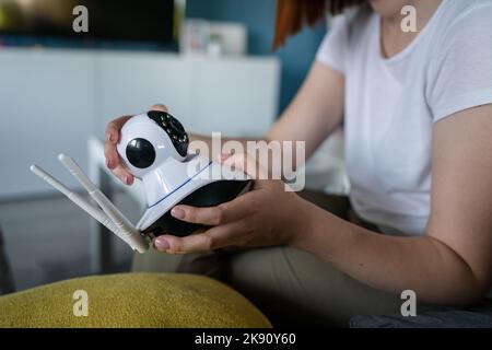 Primo piano sulle mani di una donna caucasica sconosciuta che tiene la telecamera di sorveglianza di sicurezza a casa mentre si siede sul letto a casa sua in sala regolazione e set Foto Stock