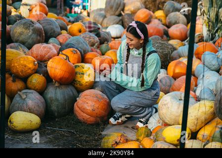 La donna contadina in una tuta di denim sceglie la zucca matura Foto Stock