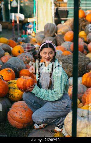 La donna contadina in una tuta di denim sceglie la zucca matura Foto Stock