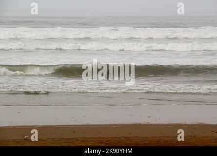 Un solista che entra onde infrangenti su un ventoso ottobre pomeriggio Playa de San Lorenzo Gijon Asturias Spagna Foto Stock