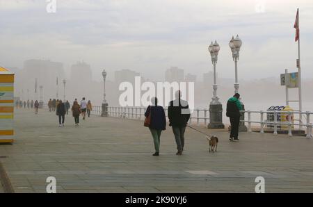 Persone che camminano su una nebbia ventosa ottobre pomeriggio sul lungomare vicino alla Playa de San Lorenzo Gijon Asturias Spagna Foto Stock