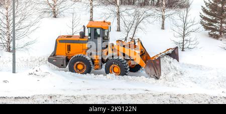 Sgombero neve. Il trattore si stacca dopo un'intensa nevicata. Un grande trattore arancione rimuove la neve dalla strada e libera il marciapiede. Pulizia delle strade Foto Stock