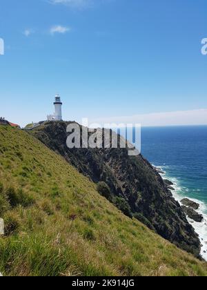 Un basso angolo verticale del faro di Capo Byron sulla collina coperta di erba, mare intorno, cielo trasparente sfondo Foto Stock