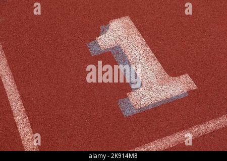 Prima corsia su una pista da atletica che mostra un numero uno dipinto sul terreno di gomma rossa Foto Stock