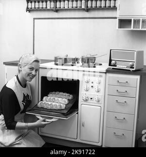 In cucina nel 1950s. Una giovane donna in cucina che prende il pane pronto al forno. In cima pentole e padelle in acciaio inossidabile, un materiale che divenne popolare dopo l'era dell'alluminio. Svezia 1959 Ref Kristoffersson CQ97-6 Foto Stock