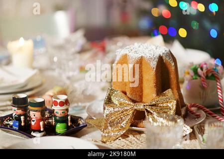 Torta di Natale Pandoro italiana decorata con nastro d'oro su un tavolo con assortite decorazioni natalizie per celebrare le festività natalizie Foto Stock