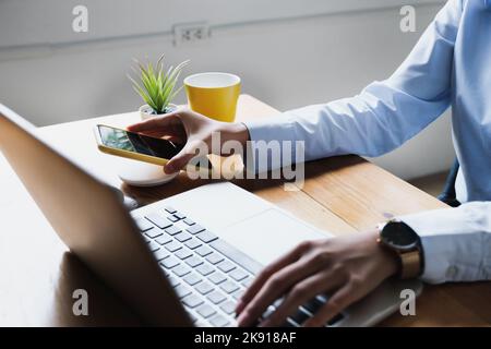 Focus femmina che tiene lo smartphone in mano per la ricarica tramite il pad di ricarica rapida wireless al lavoro. Tono vintage. Foto Stock