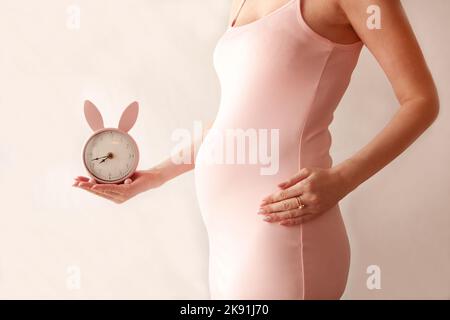Affascinante pancia-pancia che donna incinta in vestito rosa con coniglietto orologio Foto Stock