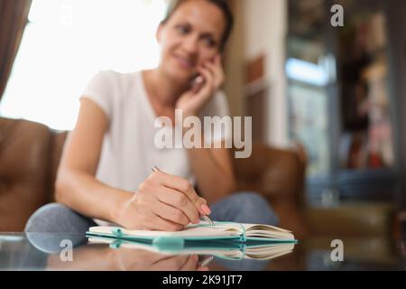 Donna che parla al telefono e scrive qualcosa sul blocco note Foto Stock