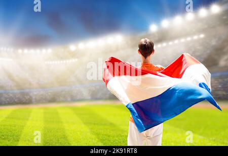Olandese tifoso di calcio sullo stadio. Tifosi olandesi sul campo da calcio guardando la squadra giocare. Giocatore o fan con bandiera e maglia nazionale Foto Stock