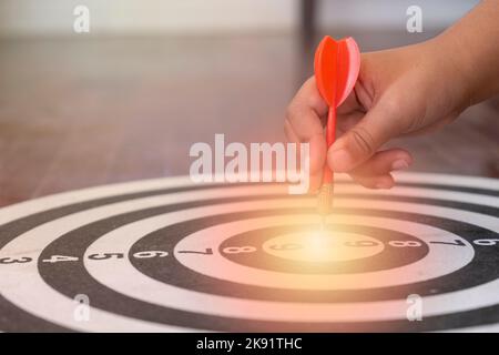 Un primo piano di una mano che tiene una freccetta sopra il bersaglio con una luce Foto Stock