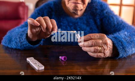 Donna di età caucasica che tiene un tampone di cotone per il naso per raccogliere un possibile campione COVID-19 positivo durante la pandemia. Nonna che usa il test dell'antigene Foto Stock