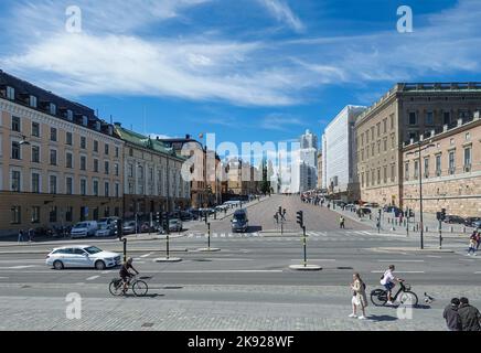 Svezia, Stoccolma - 17 luglio 2022: Guarda Slotesbacken dal molo di Skeppsbron. Palazzo reale om a destra, sotto il paesaggio azzurro. Pedoni, biciclette e c Foto Stock