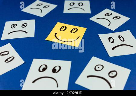 Note appiccicose con faccia Smiley disegnata a mano e facce tristi su sfondo blu. Concetto positivo di modo di pensare. Positivo vince negativo Foto Stock