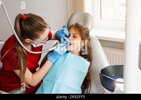 Il dentista del bambino fa la pulizia professionale dei denti in odontoiatria. Igiene professionale per i denti del bambino in odontoiatria. Il dentista pediatrico esamina e con Foto Stock