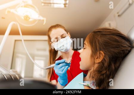 Il dentista del bambino fa la pulizia professionale dei denti in odontoiatria. Igiene professionale per i denti del bambino in odontoiatria. Il dentista pediatrico esamina e con Foto Stock