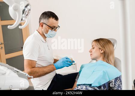 Protesi dentaria consultazione con dentista per paziente donna in odontoiatria. Il dentista medico mostra la mascella plastica artificiale con gli impianti dentali Foto Stock