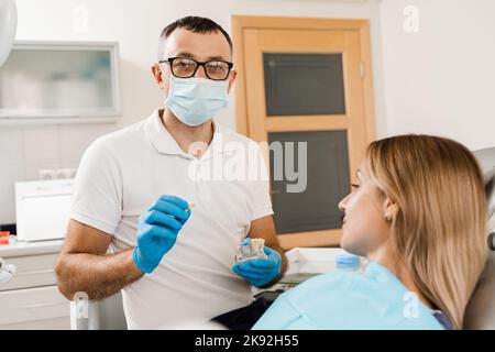 Protesi dentaria consultazione con dentista per paziente donna in odontoiatria. Il dentista medico mostra la mascella plastica artificiale con gli impianti dentali Foto Stock