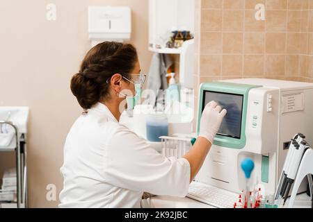 L'assistente di laboratorio lavora sull'analizzatore di sangue ed esegue analisi ematologiche in laboratorio. Apparecchiature mediche in laboratorio. Biochimica ed ematolo Foto Stock