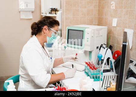 L'assistente di laboratorio lavora sull'analizzatore di sangue ed esegue analisi ematologiche in laboratorio. Apparecchiature mediche in laboratorio. Biochimica ed ematolo Foto Stock