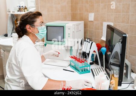 L'assistente di laboratorio lavora sull'analizzatore di sangue ed esegue analisi ematologiche in laboratorio. Apparecchiature mediche in laboratorio. Biochimica ed ematolo Foto Stock
