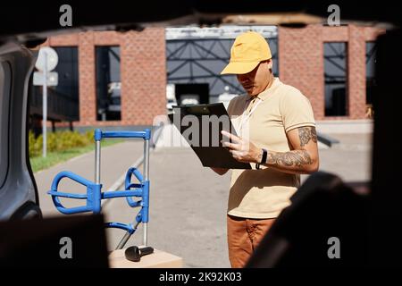 Ritratto di un operatore multietnico che compila i moduli mentre si trova in piedi da un furgone alla luce del sole, in uno spazio di copia Foto Stock