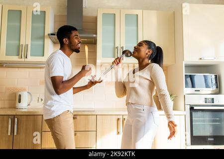 coppia ispanica cantando insieme tenendo un mestolo come un microfono in cucina Foto Stock