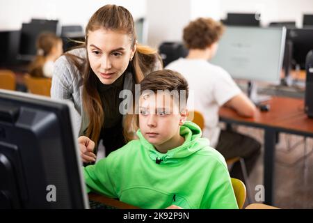 L'insegnante insieme agli studenti conduce una lezione sull'educazione informatica Foto Stock