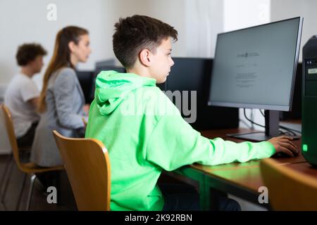 Ha messo a fuoco il ragazzo di Tween che studia con i compagni di classe in laboratorio del calcolatore Foto Stock