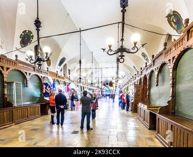 CRACOVIA, POLONIA - 4 MAGGIO: Persone in transito con bancarelle di souvenir artigianali della sala di stoffa gotica Sukiennice sulla piazza del mercato principale il 5 maggio, Foto Stock