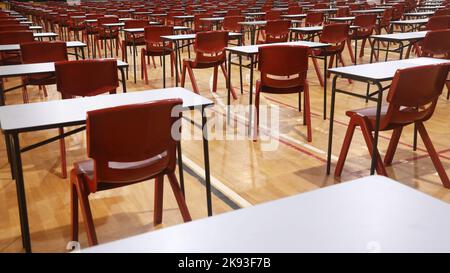 Vista di una sala d'esame per studenti delle scuole superiori o superiori allestita e organizzata in file ordinate di tavoli o scrivanie per esami e sedie rosse. Foto Stock