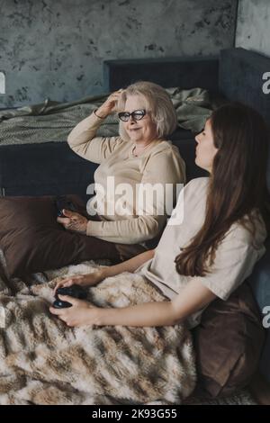 Nonna sorridente che gioca o con sua figlia sul computer, trascorrendo del tempo insieme. Vittoria del gioco. Joystick di gioco moderno. Famiglia felice. Foto Stock