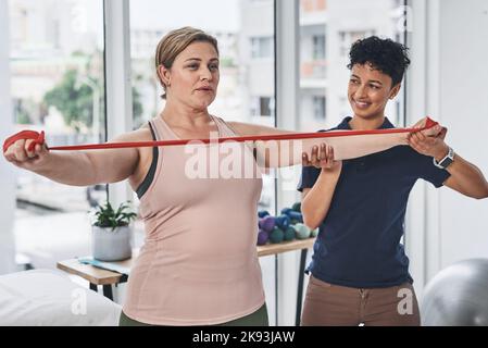 Questo esercizio aiuta a migliorare la capacità articolare e la gamma di movimento. Un giovane fisioterapista aiuta il paziente maturo ad esercitare con una fascia di resistenza a Foto Stock