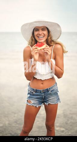 Raffreddando giù con una certa frutta. Ritratto ritagliato di una giovane donna attraente in piedi e giocosamente tenere un pezzo di anguria durante una vacanza. Foto Stock