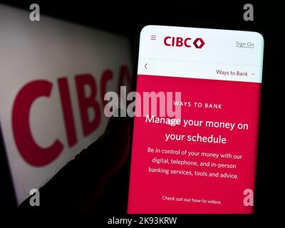 Persona che tiene in mano uno smartphone con il sito Web della Canadian Imperial Bank of Commerce (CIBC) sullo schermo davanti al logo. Messa a fuoco al centro del display del telefono. Foto Stock