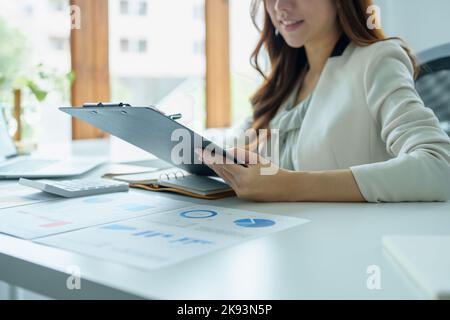 Un ritratto di una donna d'affari in possesso di un documento di bilancio e utilizzando computer e calcolatrici posti su una scrivania per analizzare gli investimenti per gestire i rischi in Foto Stock