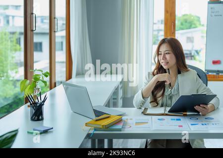 Un ritratto di una donna d'affari in possesso di un documento di bilancio e utilizzando computer e calcolatrici posti su una scrivania per analizzare gli investimenti per gestire i rischi in Foto Stock