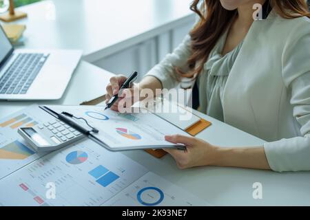 Un ritratto di una donna d'affari in possesso di un documento di bilancio e utilizzando computer e calcolatrici posti su una scrivania per analizzare gli investimenti per gestire i rischi in Foto Stock