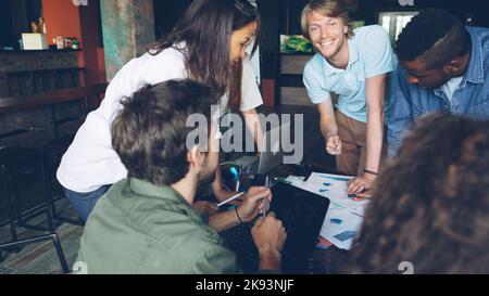 Un gruppo di giovani colleghi sta discutendo grafici e grafici in piedi intorno al tavolo in un ufficio moderno. Business, lavoro di squadra di successo e concetto di professionisti. Foto Stock
