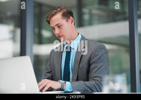 Rispondere alle e-mail aziendali. Un bel giovane uomo d'affari seduto da solo in ufficio e a digitare sul computer portatile. Foto Stock