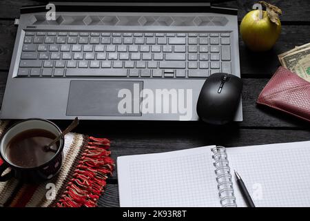 la tazza nera del blocco note del laptop con i soldi del caffè si trovano sul tavolo nero di legno di lavoro, sul laptop sul tavolo di lavoro durante il lavoro, sul processo creativo, sul freelance Foto Stock