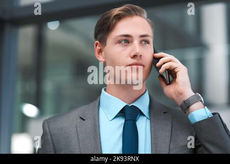 Sigilla l'affare sopra il telefono. Un giovane imprenditore bello che si alza da solo nel suo ufficio e che usa il suo cellulare. Foto Stock