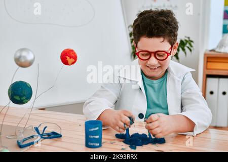 Sappiamo tutti che fare un pasticcio è sempre divertente: Un adorabile giovane ragazzo che gioca e sperimenta il slime nella classe scientifica a scuola. Foto Stock