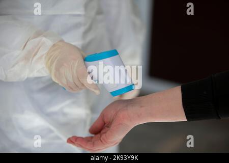 Un medico utilizza una pistola termometro per esterni per controllare la temperatura corporea per i sintomi del virus covid-19. Foto Stock