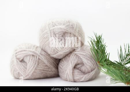 Matasse di lana grigia di filato caldo su fondo bianco con ramo di abete rosso. Verticale. Lavorazione a maglia, hobby. Spazio di copia Foto Stock