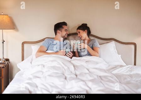 Abbiamo sempre qualcosa di cui parlare: Una giovane coppia felice che beve il caffè a letto nella loro camera da letto a casa. Foto Stock